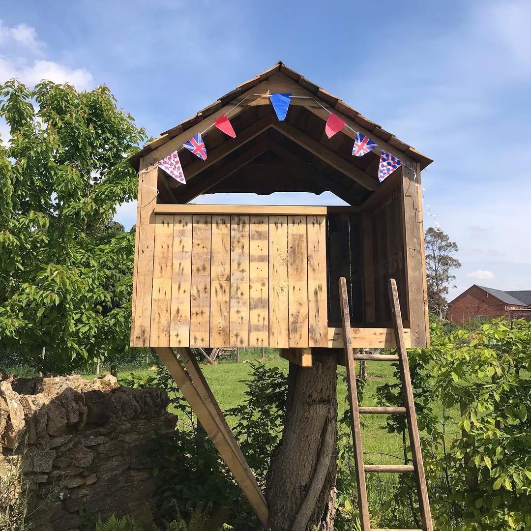 Finished pallet-wood treehouse with pitched shingle roof and bunting